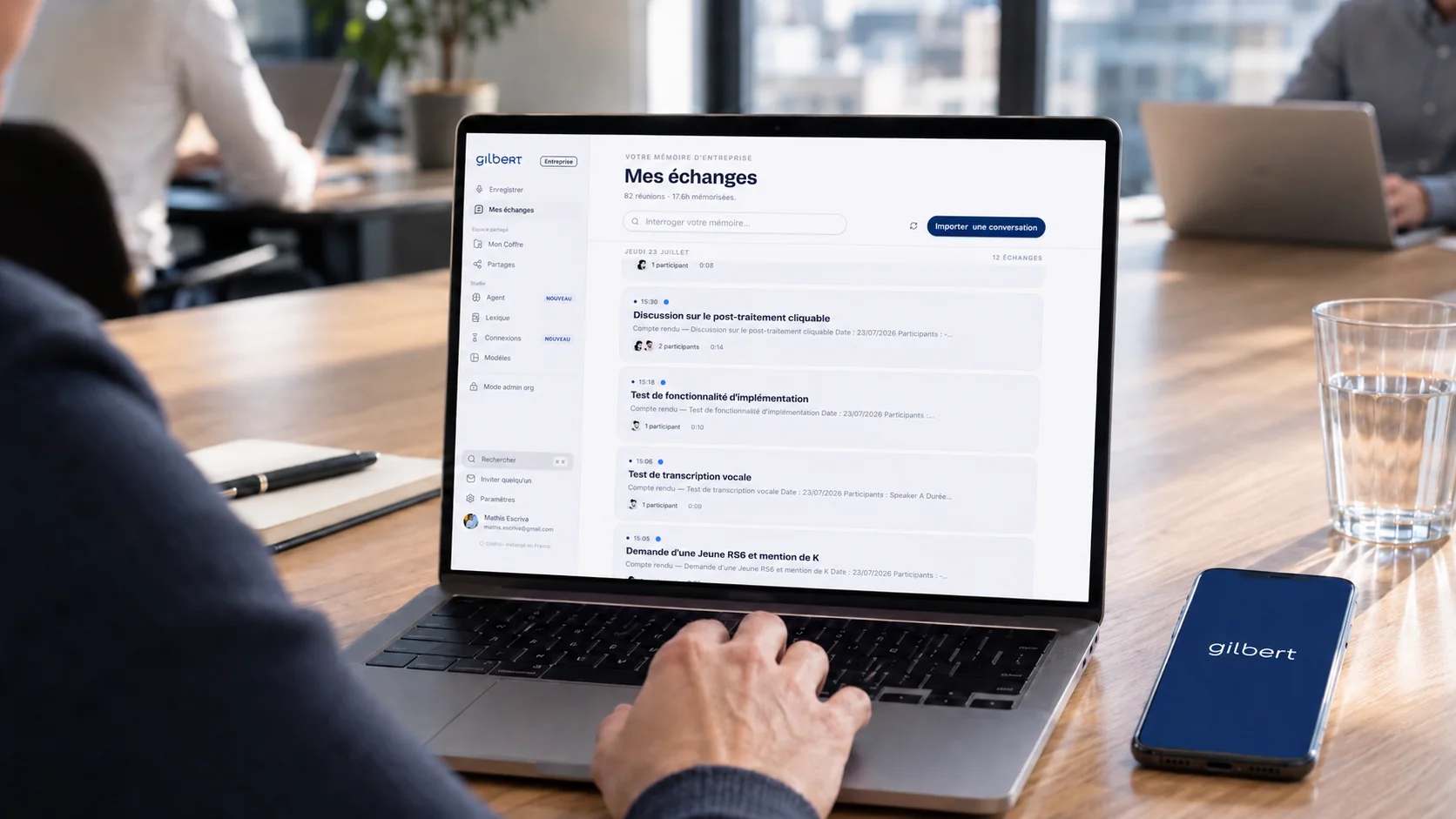 Gilbert en réunion : la mémoire d'entreprise « Mes échanges » ouverte sur un MacBook, l'app mobile posée à côté